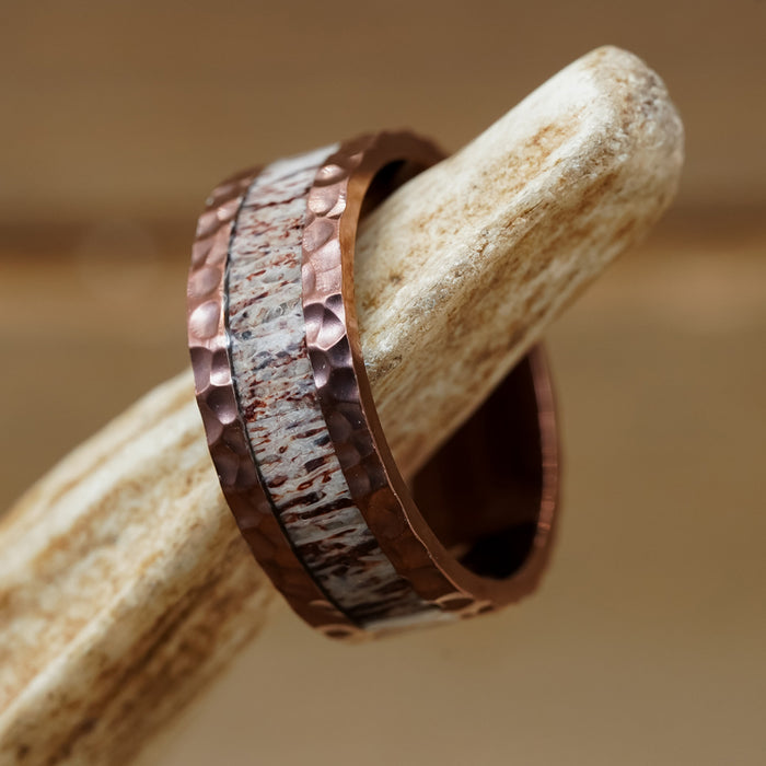 The Mount Vinson, a hammered copper ring featuring a textured silver inlay reminiscent of a men's wedding band, rests on a light-colored, bone-like object.