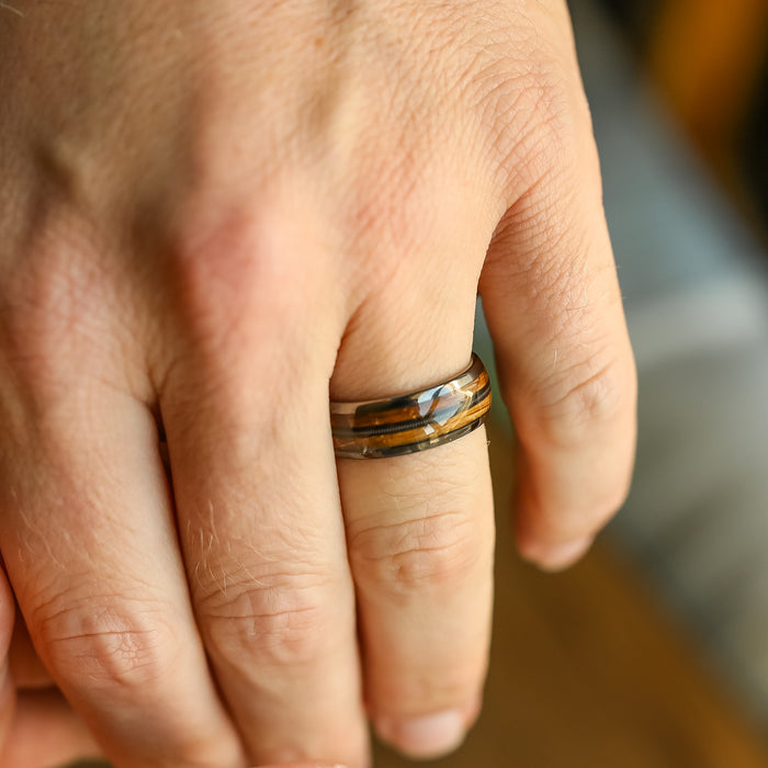 A close-up of a left hand wearing The Nashville, a unique guitar string ring featuring a marbled pattern of brown, black, and silver colors on the ring finger.