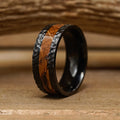 Introducing The Nickerson: a striking men's wedding band, this hand-hammered ring features a black titanium band with a unique hammered texture and a central inlay of polished brown wood grain, elegantly resting on a wooden surface.