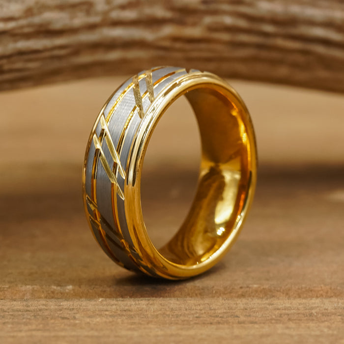 The Ogden, featuring a gold striped band with a matte silver inlay and engraved diagonal lines, is displayed upright on a wooden surface against a blurred wooden background.