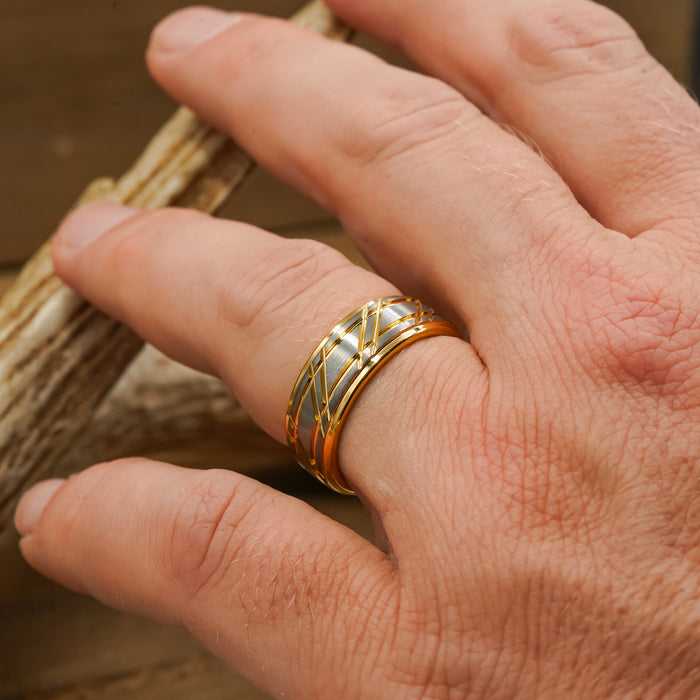 A close-up of a hand wearing The Ogden, a gold striped band with intricate wire detailing, touching a piece of light-colored wood.