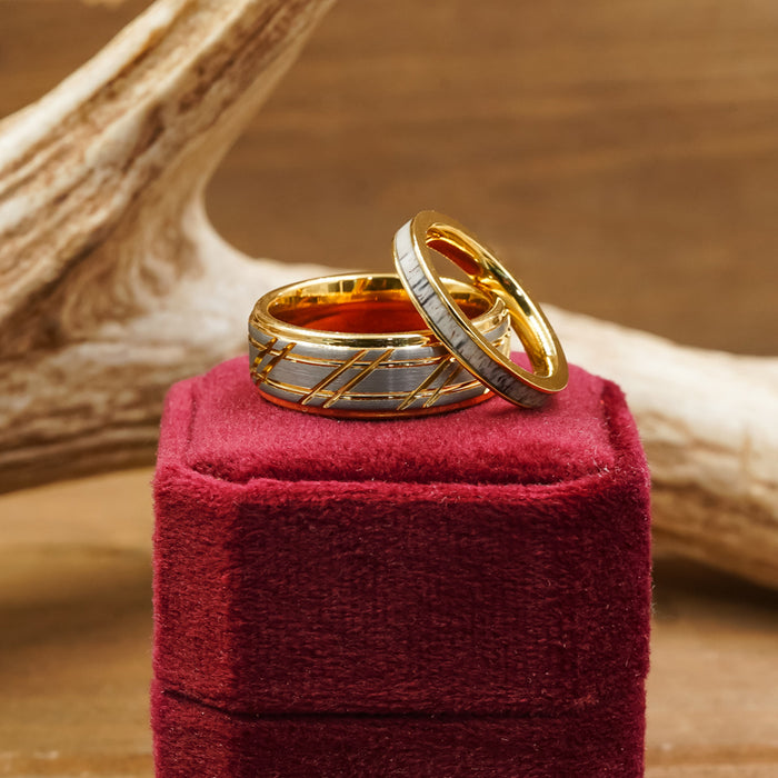 Two gold and silver rings, including The Ogden: a gold striped band, rest atop a red velvet ring box, with a wooden antler decoration softly blurred in the background.