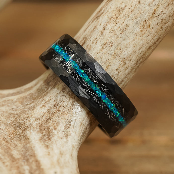 The Palo Verde, a black tungsten carbide ring featuring a faceted surface and a blue-green iridescent inlay, rests on a textured, light-colored antler.