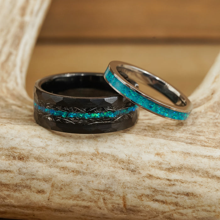 Two rings rest on a textured ivory surface: The Palo Verde, a wide tungsten carbide ring featuring a striking blue-green inlay reminiscent of green opal, and a narrower silver ring adorned with a matching blue-green inlay.