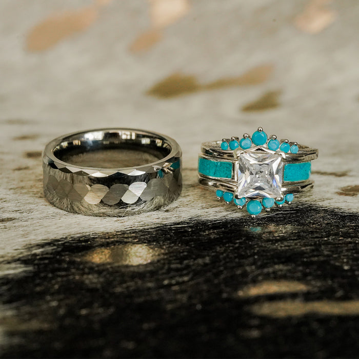 The Payson, a hammered silver ring, rests beside a dazzling silver ring adorned with a large square clear stone and delicate turquoise accents, all beautifully displayed on a textured surface.