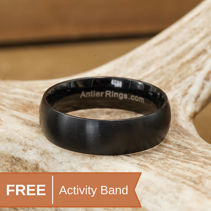 A sleek black Tungsten Carbide ring, The Ricketts Glen from AntlerRings.com, with the brand engraved inside, is displayed on a light-colored antler. Text overlay at the bottom left reads FREE Activity Band.