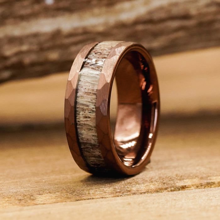 A close-up of The Sierra Nevada ring, showcasing a hammered edge with a copper-colored band and an inlay crafted from antler, resting on a wooden surface.