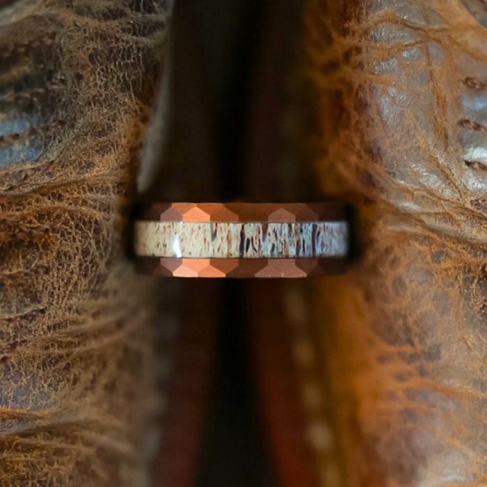 A close-up of The Sierra Nevada ring—a textured tungsten carbide band with a rugged, hammered edge—resting between two worn, brown leather surfaces.