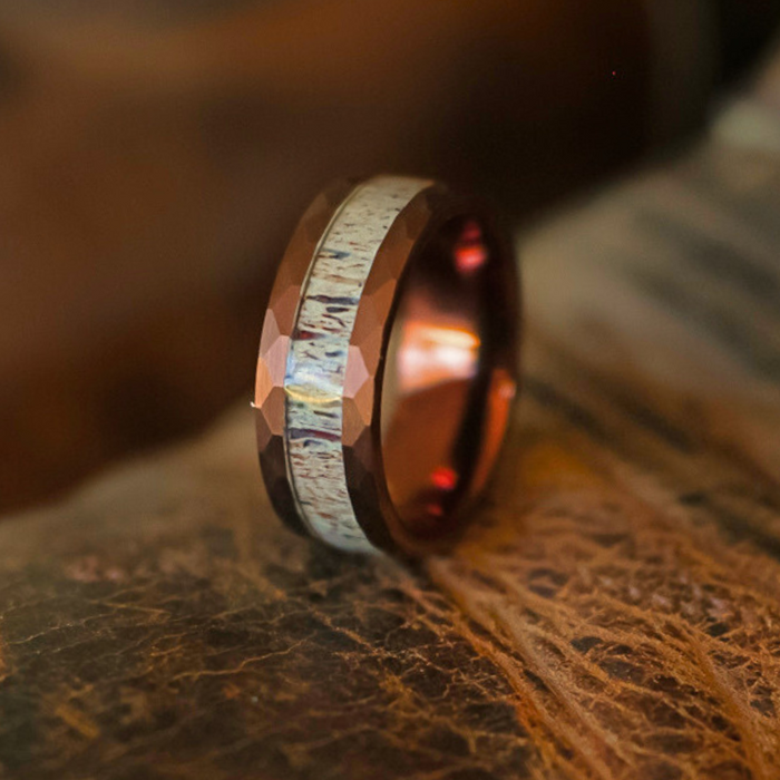 The Sierra Nevada, a Tungsten Carbide ring featuring a faceted brown finish and a textured, light-colored inlay evocative of antler, rests on a textured brown surface and is gently bathed in warm light.