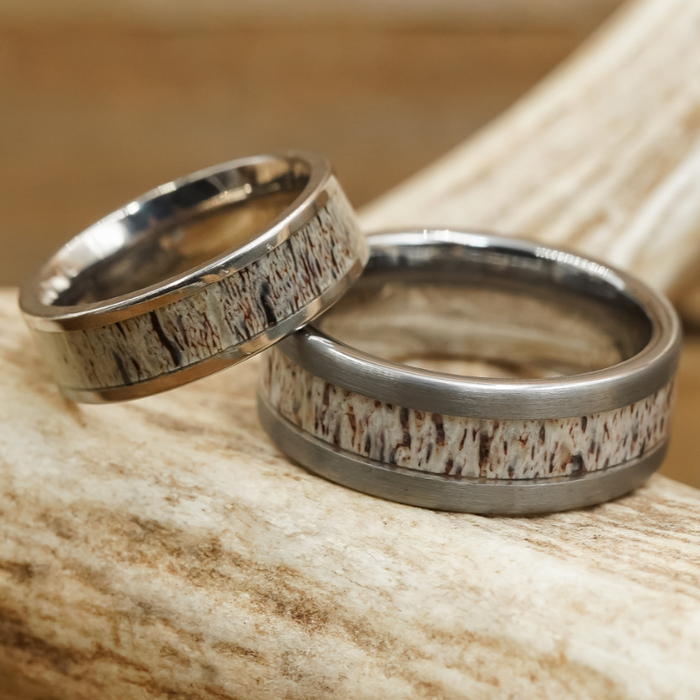 The Smoky Mountain & Sedona Couples Set features two silver rings with a rustic, textured inlay, displayed on a piece of antler that highlights the natural antler grain. One ring is slightly larger than the other, creating an ideal couples set inspired by the Smoky Mountains. Both rings showcase an earthy, organic pattern.