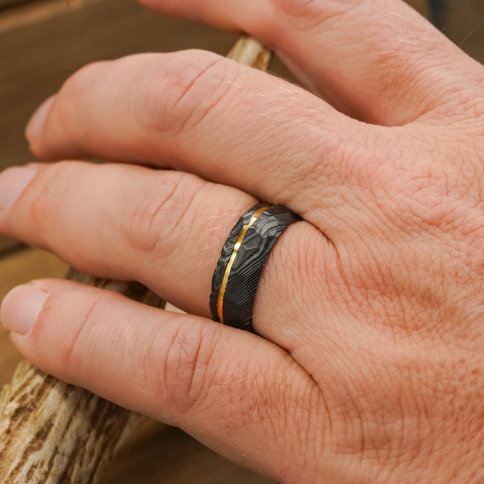 A close-up of a hand wearing The Vogel, a black hammered ring with a thin gold stripe, holding a piece of antler or wood.