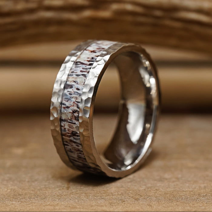 The Wilder Ranch is a men's hammered silver ring, showcasing a unique central inlay with a brown and white marbled pattern reminiscent of an antler wedding band, displayed upright on a wooden surface.